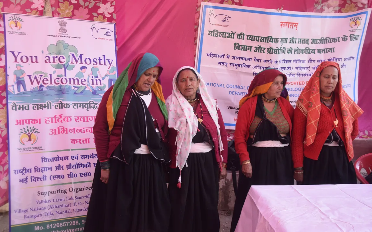 Women stand together during a folk-media programme in front of event banners.